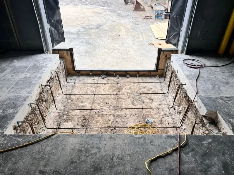 A recessed concrete loading dock pit under construction with exposed metal rebar reinforcement and wooden formwork.