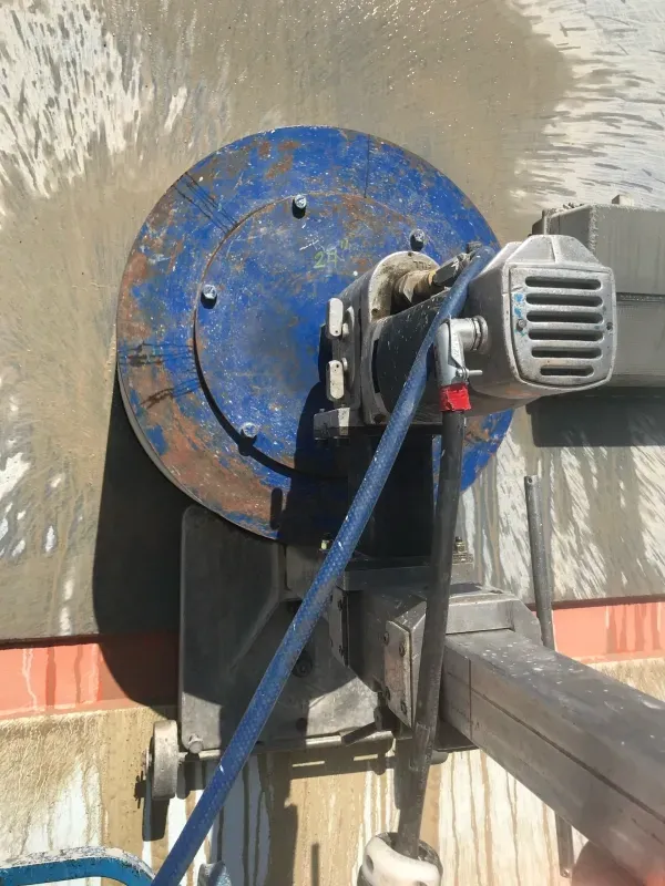 A close-up view of a blue wall-cutting saw mounted on a track, cutting into a concrete surface.