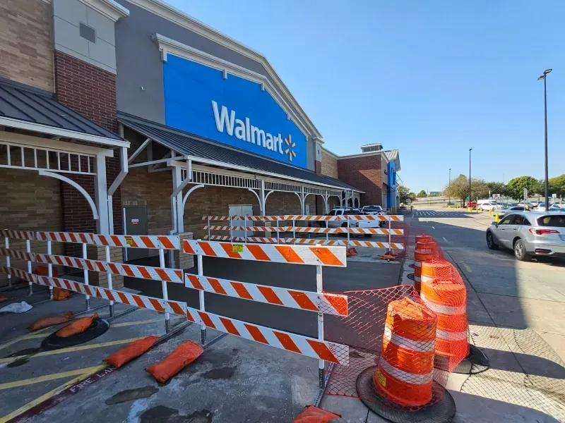 A Walmart store exterior featuring orange and white construction barricades blocking the entrance.