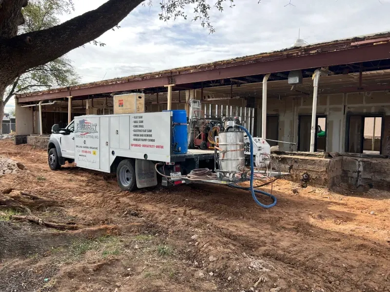A utility truck parked on a dirt lot in front of a construction site with a partially demolished building.