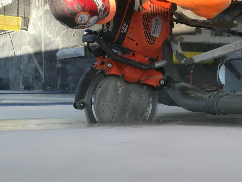 An orange walk-behind concrete saw cuts a straight line into a smooth, grey concrete floor.