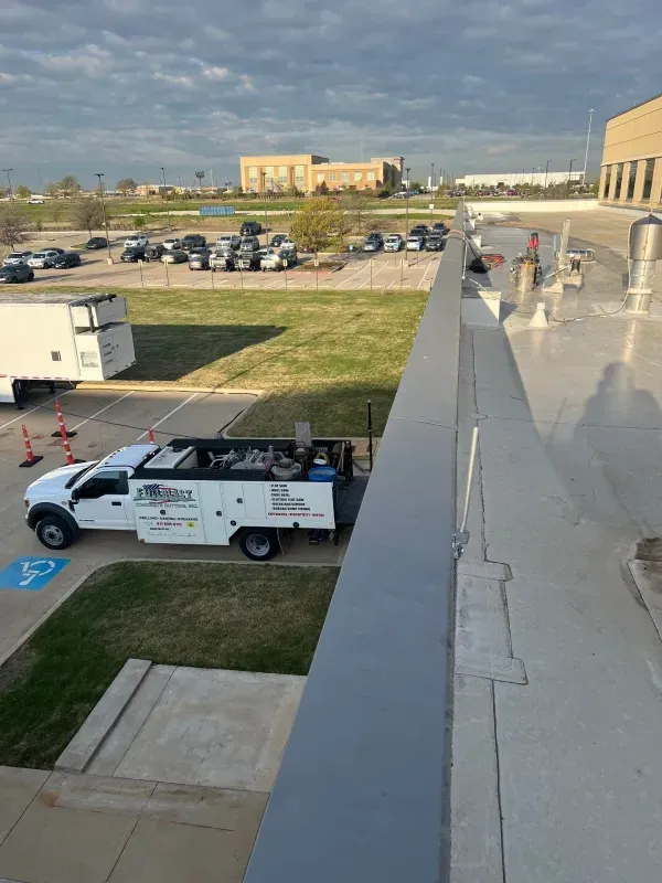 High-angle view of a parking lot with a service truck parked near a building edge under a partly cloudy sky.