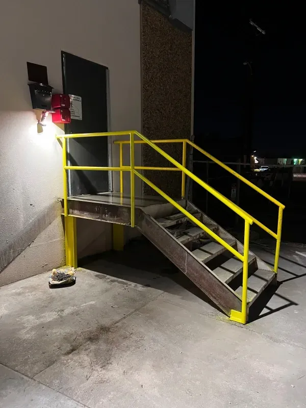 Exterior metal stairs with yellow handrails leading to an elevated doorway on a concrete surface at night.
