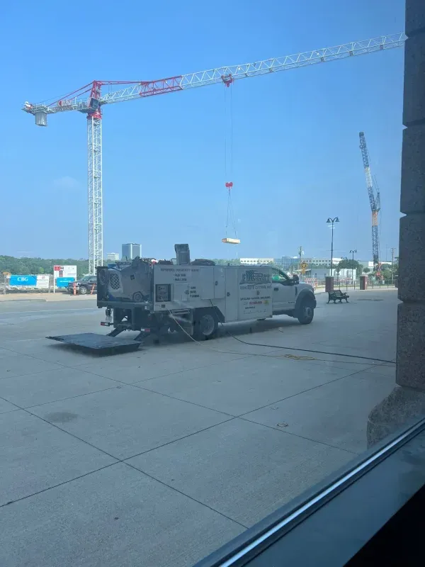A utility service truck parked on a concrete lot near a construction site with two cranes in the background.