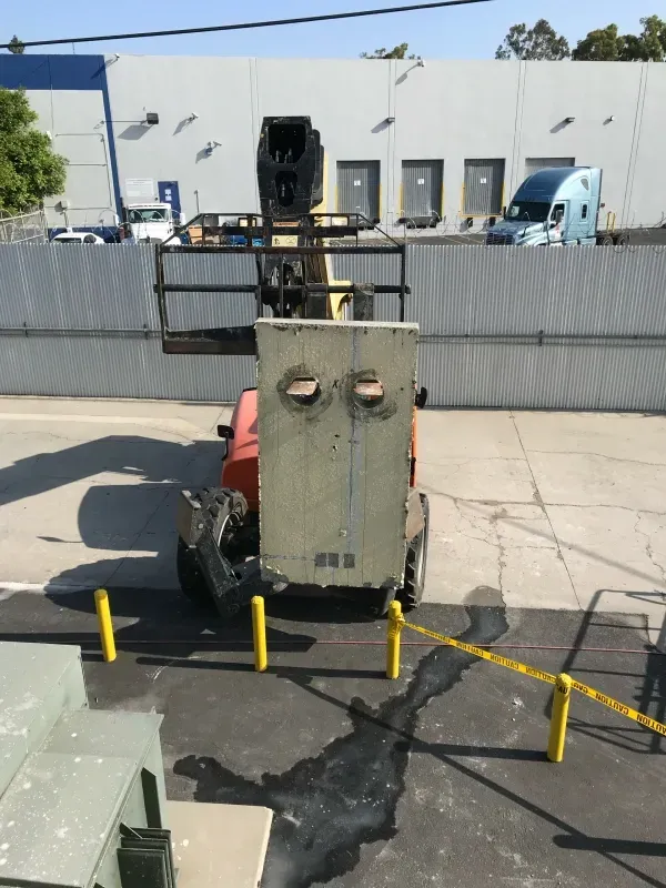 A heavy-duty orange forklift with a tall grey panel attachment is parked in an industrial yard with a metal fence.