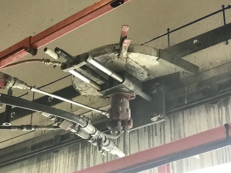 A mechanical device with a metal circular plate and hydraulic hoses attached to a ceiling structure.