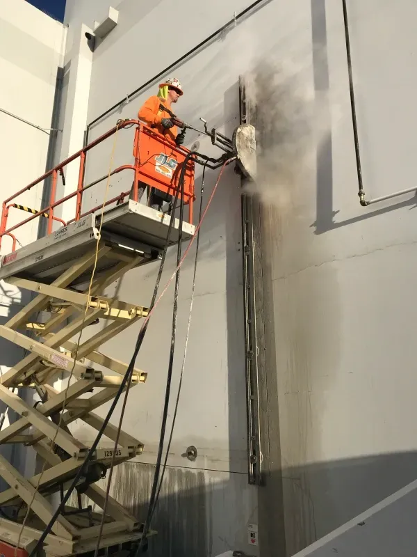 A worker in orange high-visibility gear uses a wall saw on a concrete surface while elevated on a scissor lift.