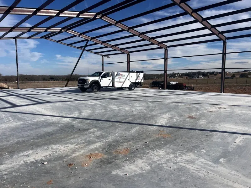 A white service truck parked on a large concrete foundation inside the metal frame of an unfinished building.