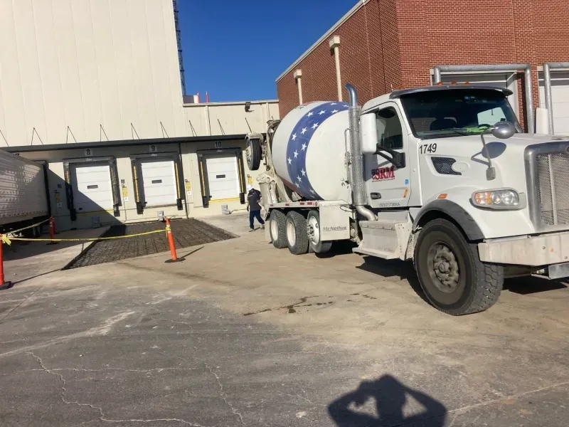 A cement mixer truck parked in a commercial loading area with several dock doors in the background.
