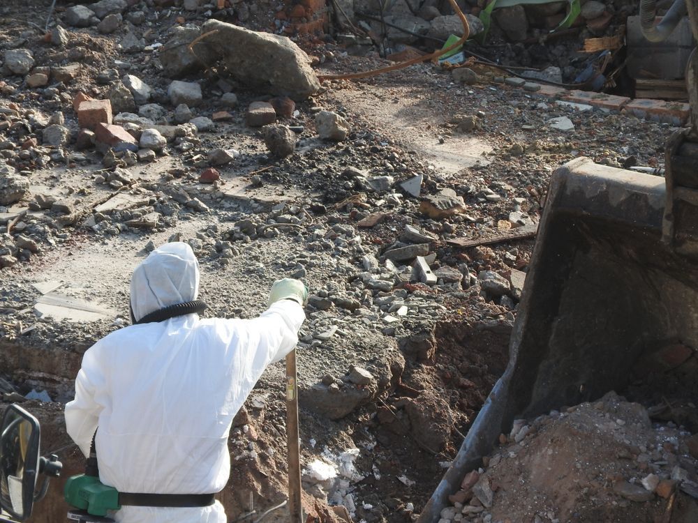 Person in White Protective Suit Examines Debris — Walsh Demolition Pty Ltd in Coffs Harbour, NSW