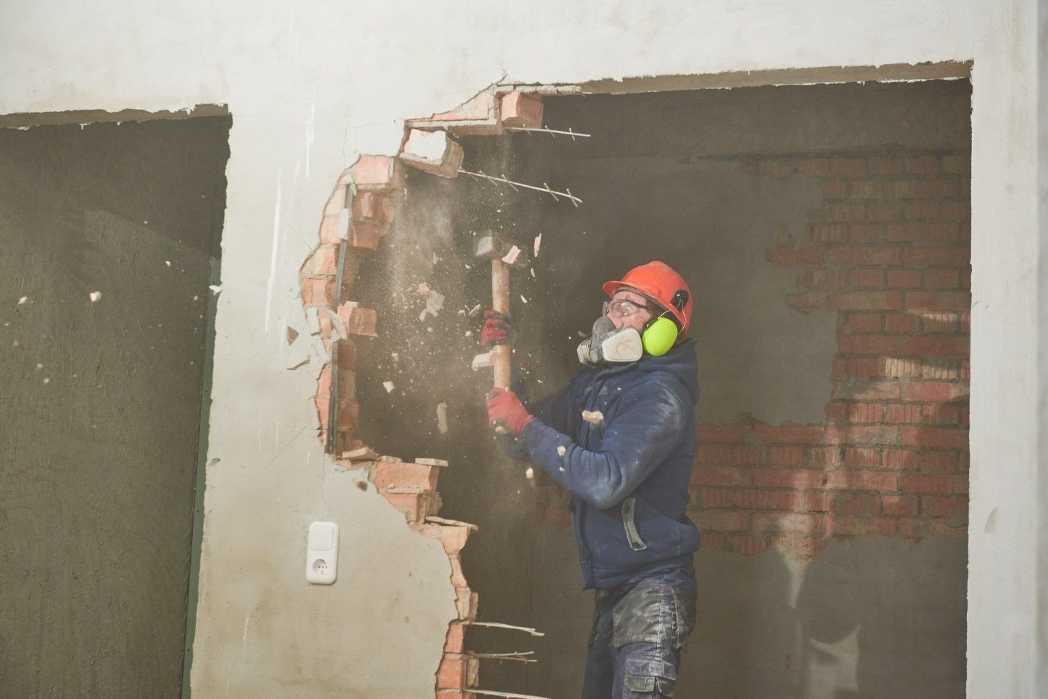 Person in Safety Gear Demolishing a Brick Wall with A Sledgehammer — Walsh Demolition Pty Ltd in Byron Bay, NSW