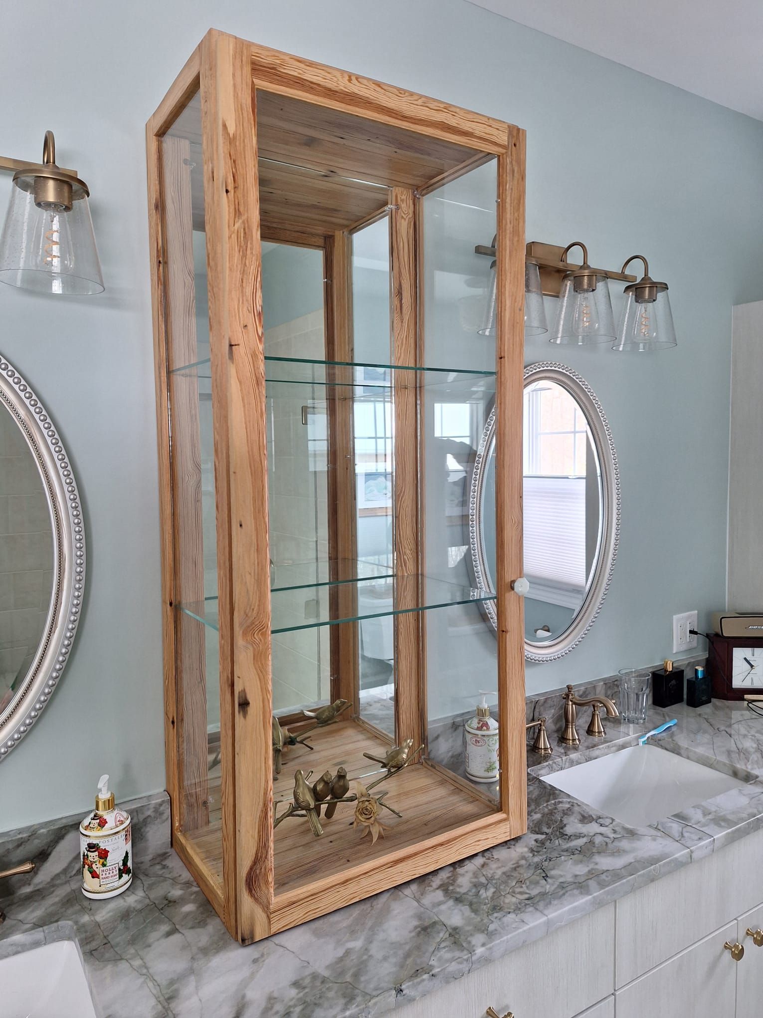 A bathroom with two mirrors and a wooden cabinet with glass doors.