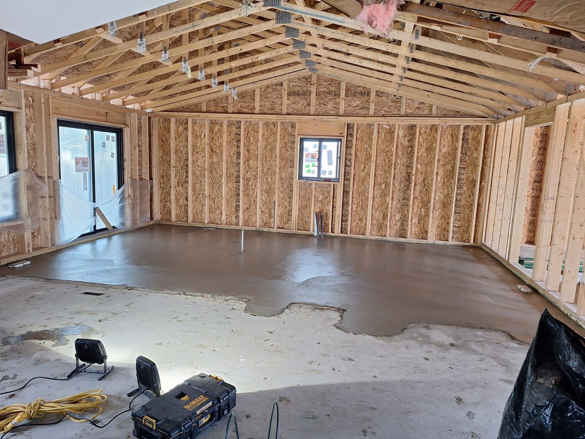 A large room with a concrete floor and wooden walls under construction.