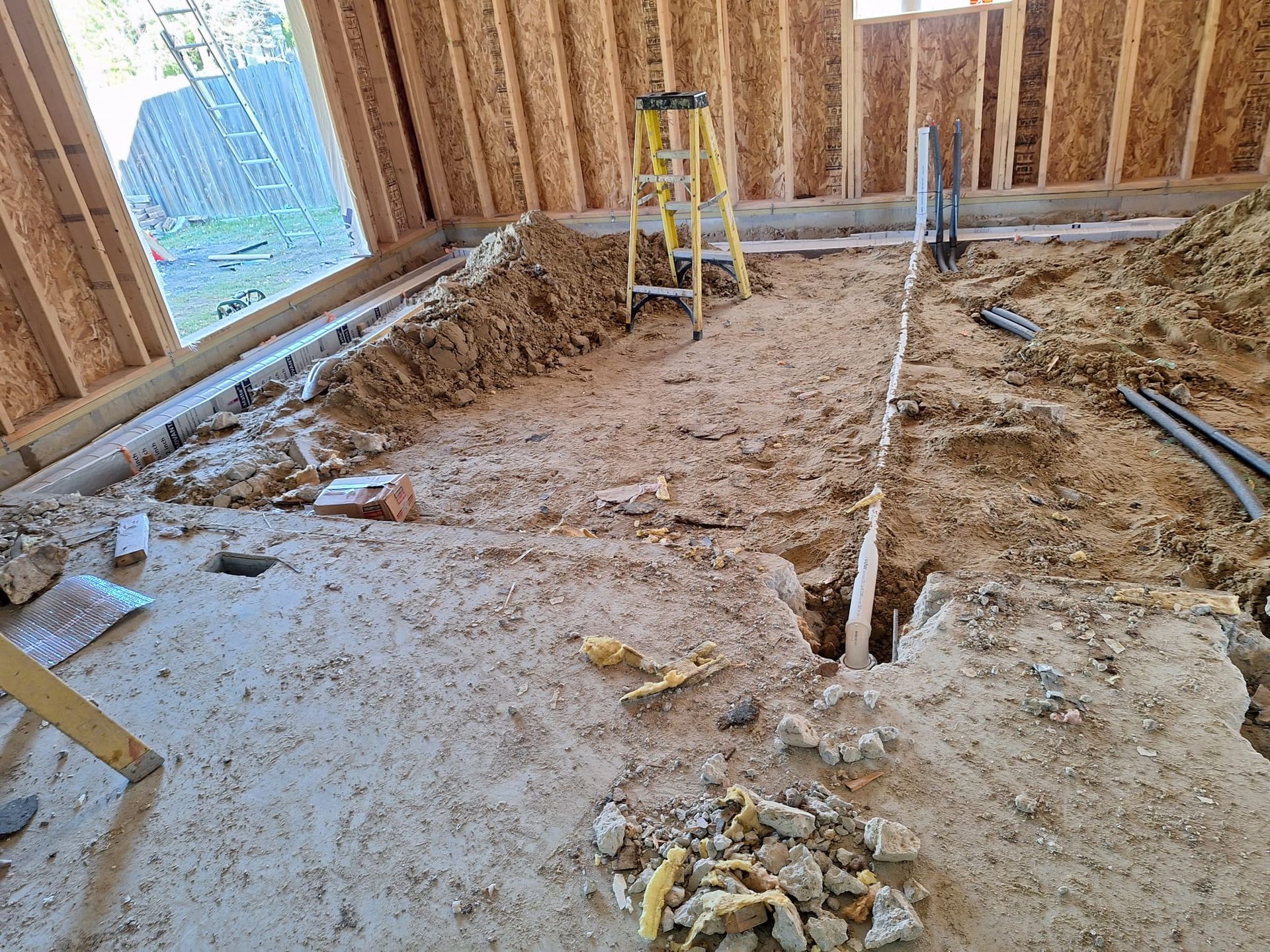 A ladder is sitting on top of a pile of dirt in a room under construction.