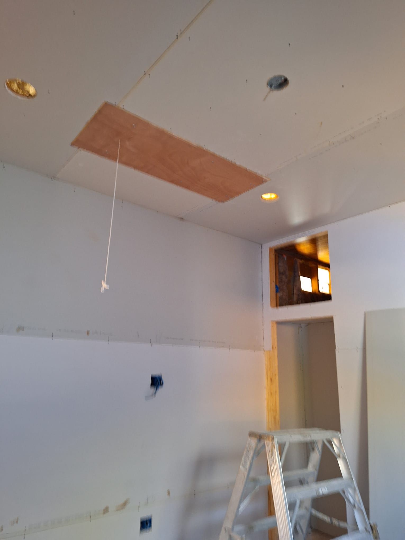A room with a ladder and a piece of wood hanging from the ceiling