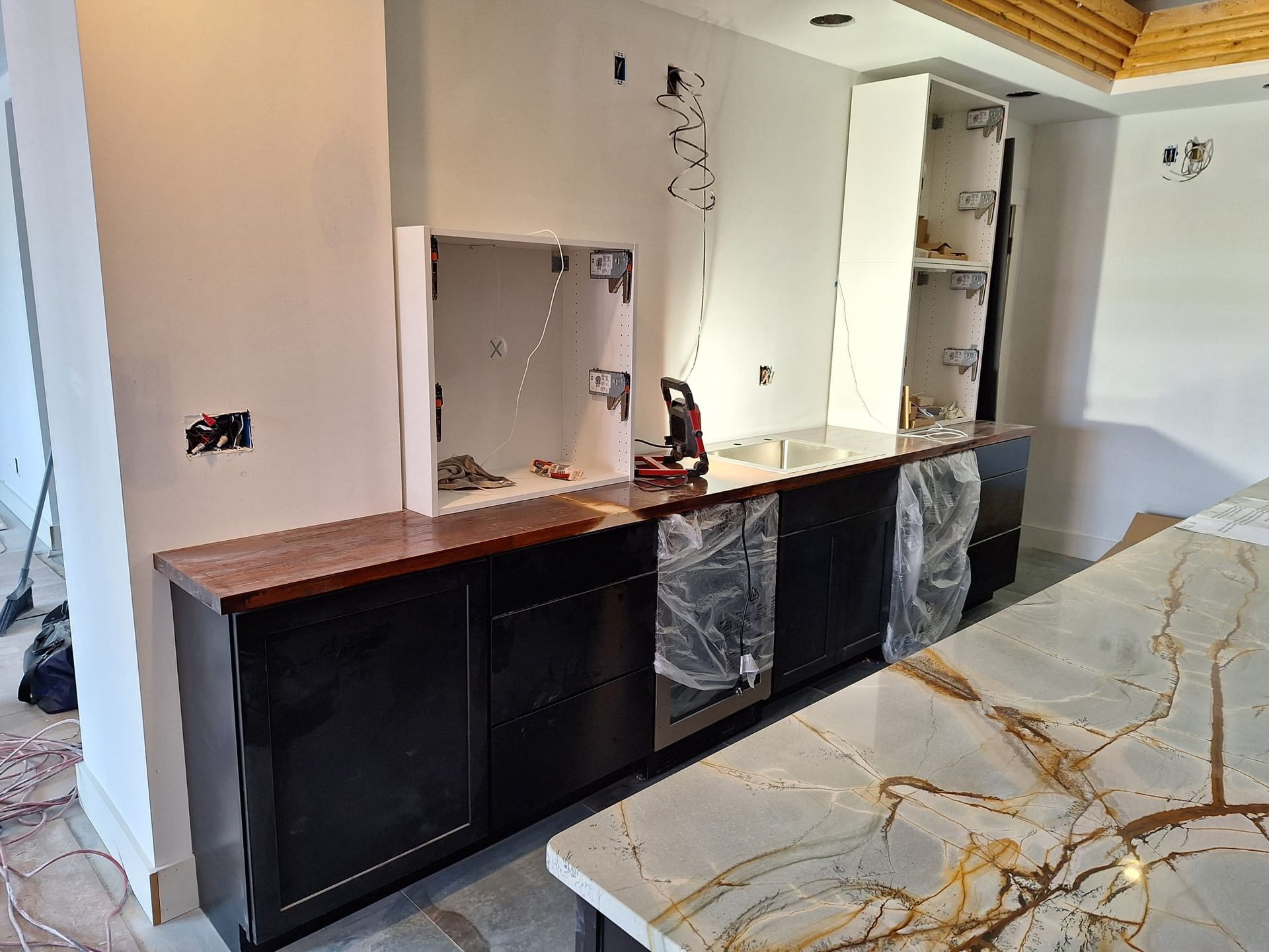 A kitchen under construction with black cabinets and marble counter tops.