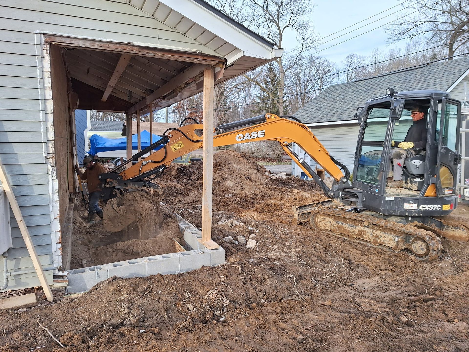 A small excavator is digging a hole in front of a house.
