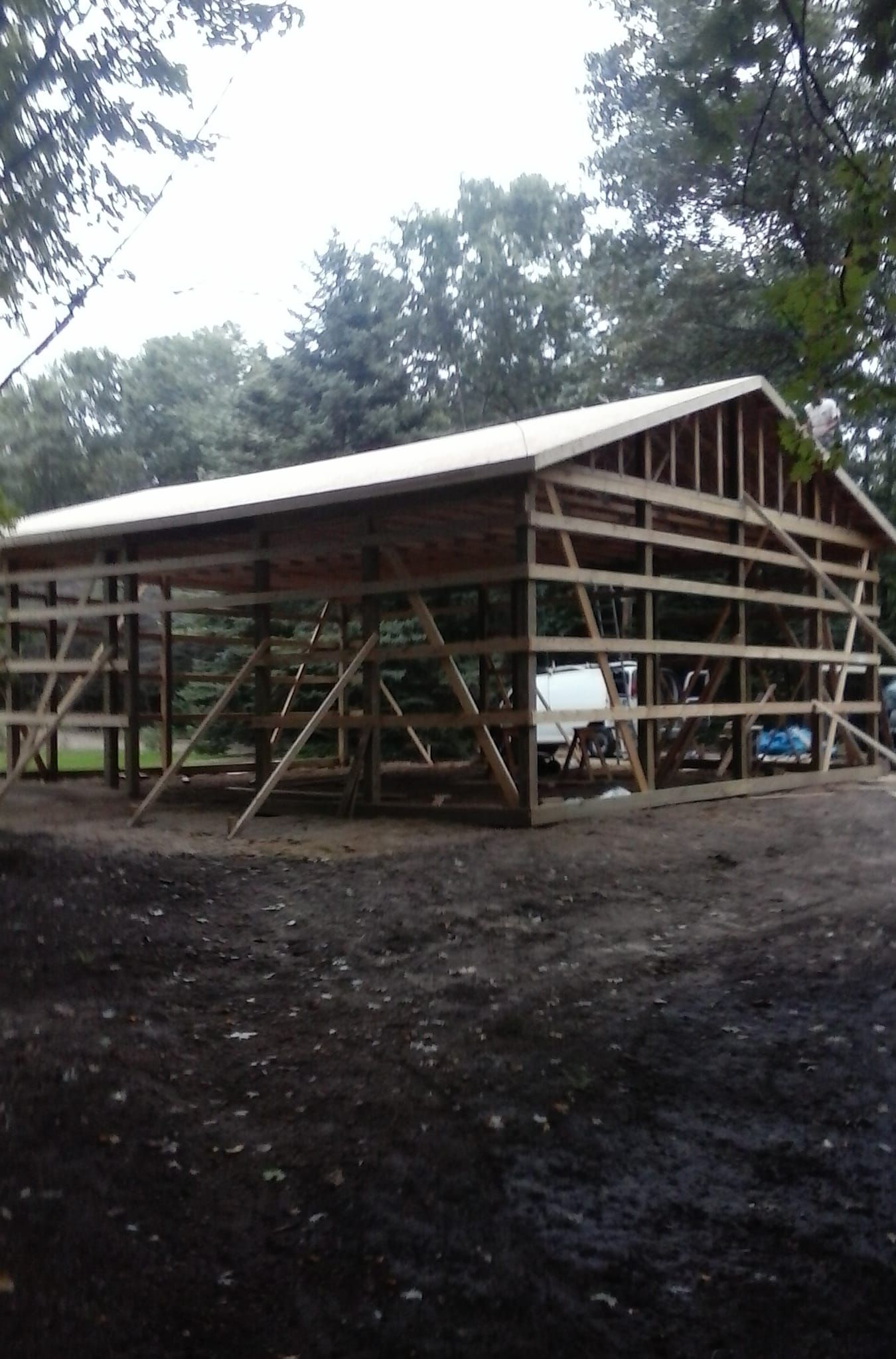 A large wooden barn is being built in the middle of a dirt field.