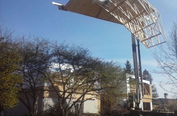 A large metal structure is being lifted by a crane in front of a house