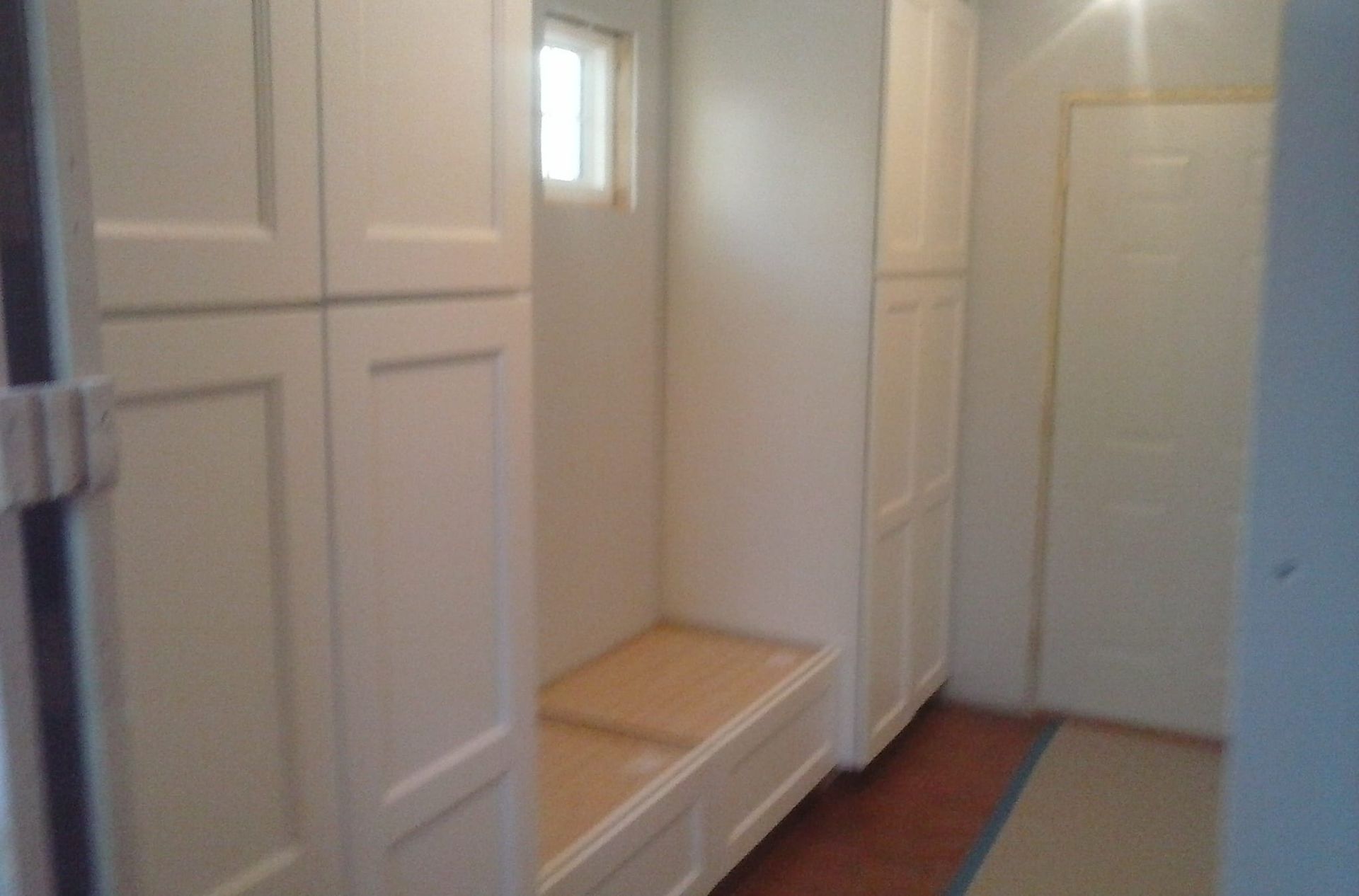 A hallway with white cabinets and a bench in the middle.