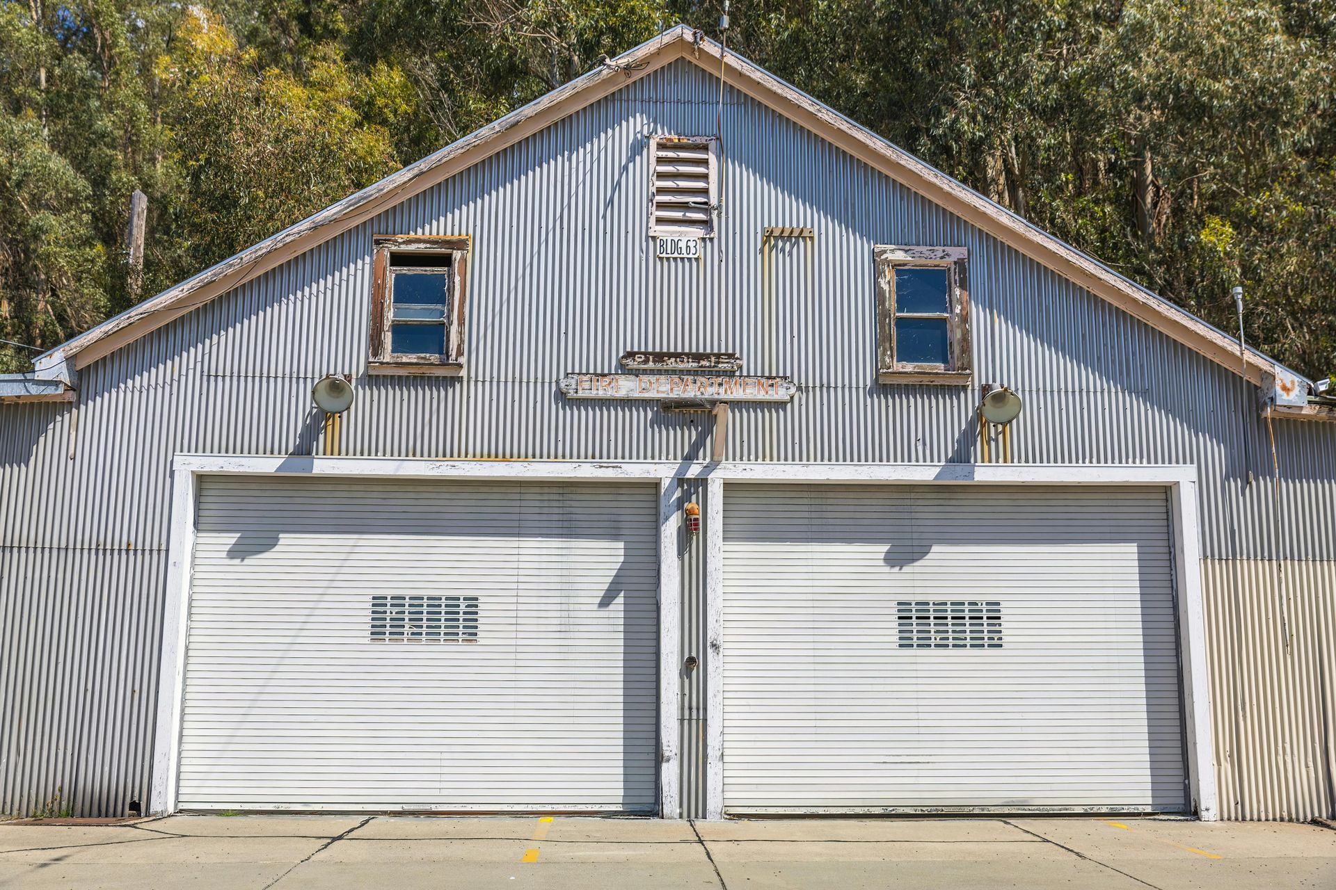 Garage with two white doors, corrugated metal siding, small windows, and weathered appearance.