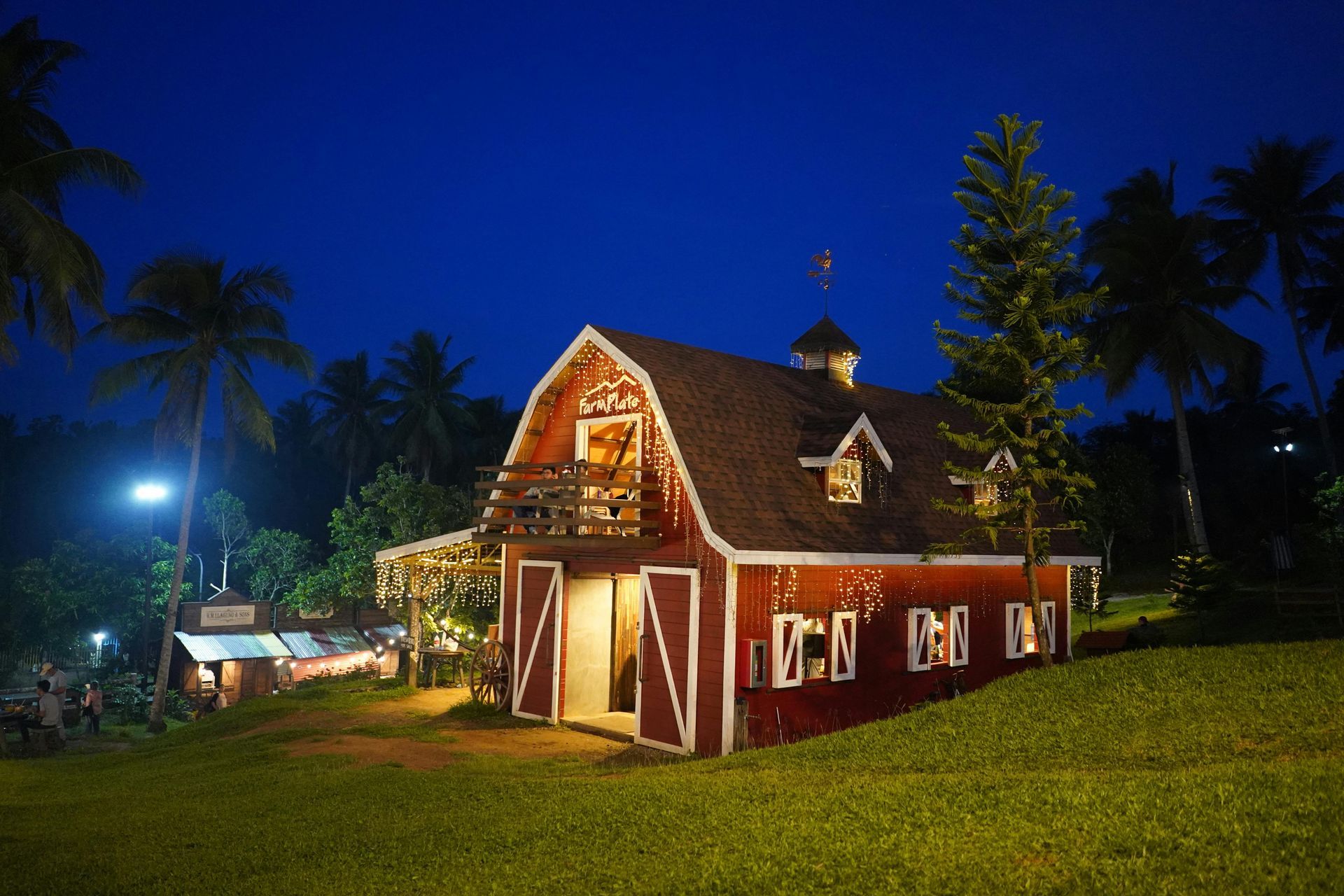 Red barn with white trim at night, surrounded by grass, trees, and dark blue sky.