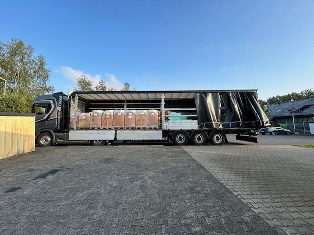 Zwarte vrachtwagen met lading, geparkeerd op een grijs wegdek. Bewolkte lucht op de achtergrond.