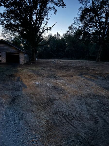 Dark yard with dirt and tractor tracks, trees and shed in background at dusk.
