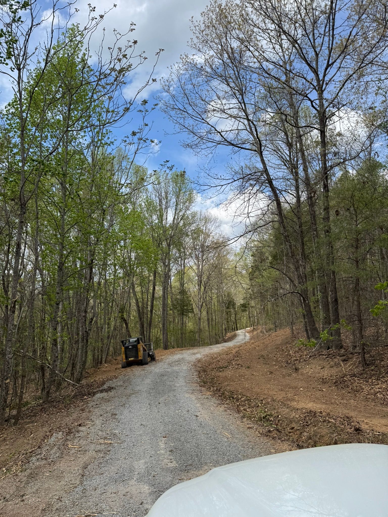 Gravel road winds through a forest with blue sky and clouds. Someone is riding a small vehicle.