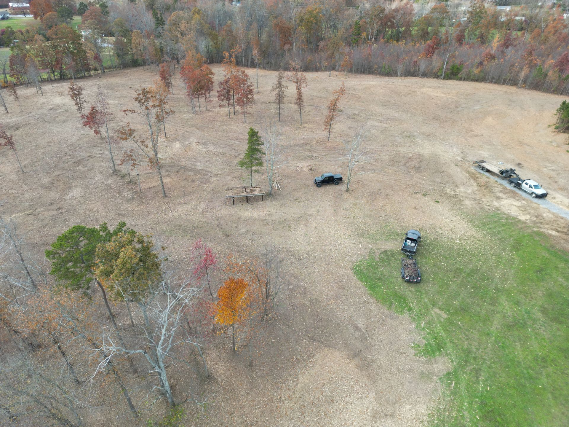 Overhead shot of a field with sparse trees and two trucks with trailers. Fall foliage colors are visible.