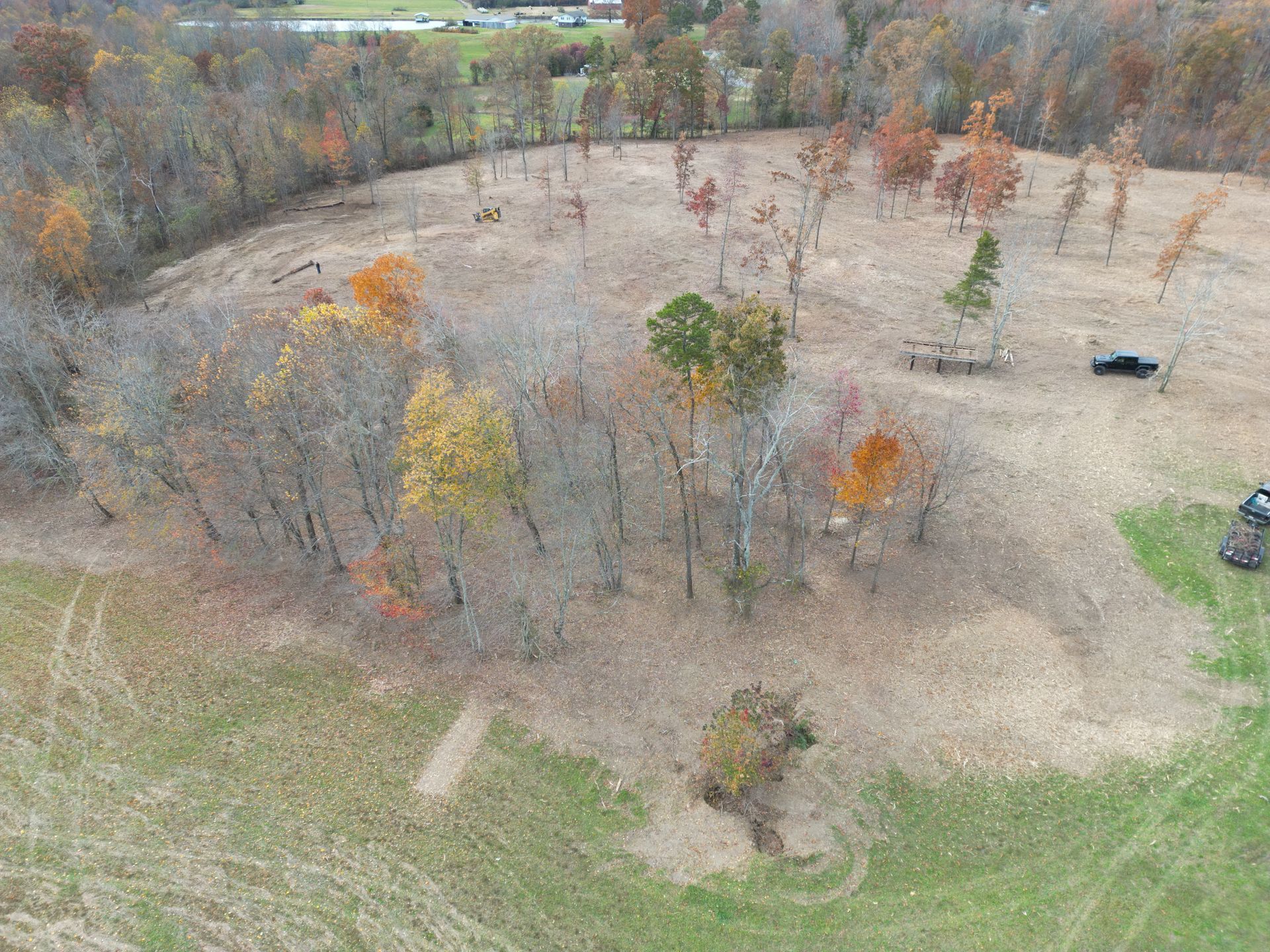 An aerial view of a mostly barren landscape with sparse trees and patches of dry grass.