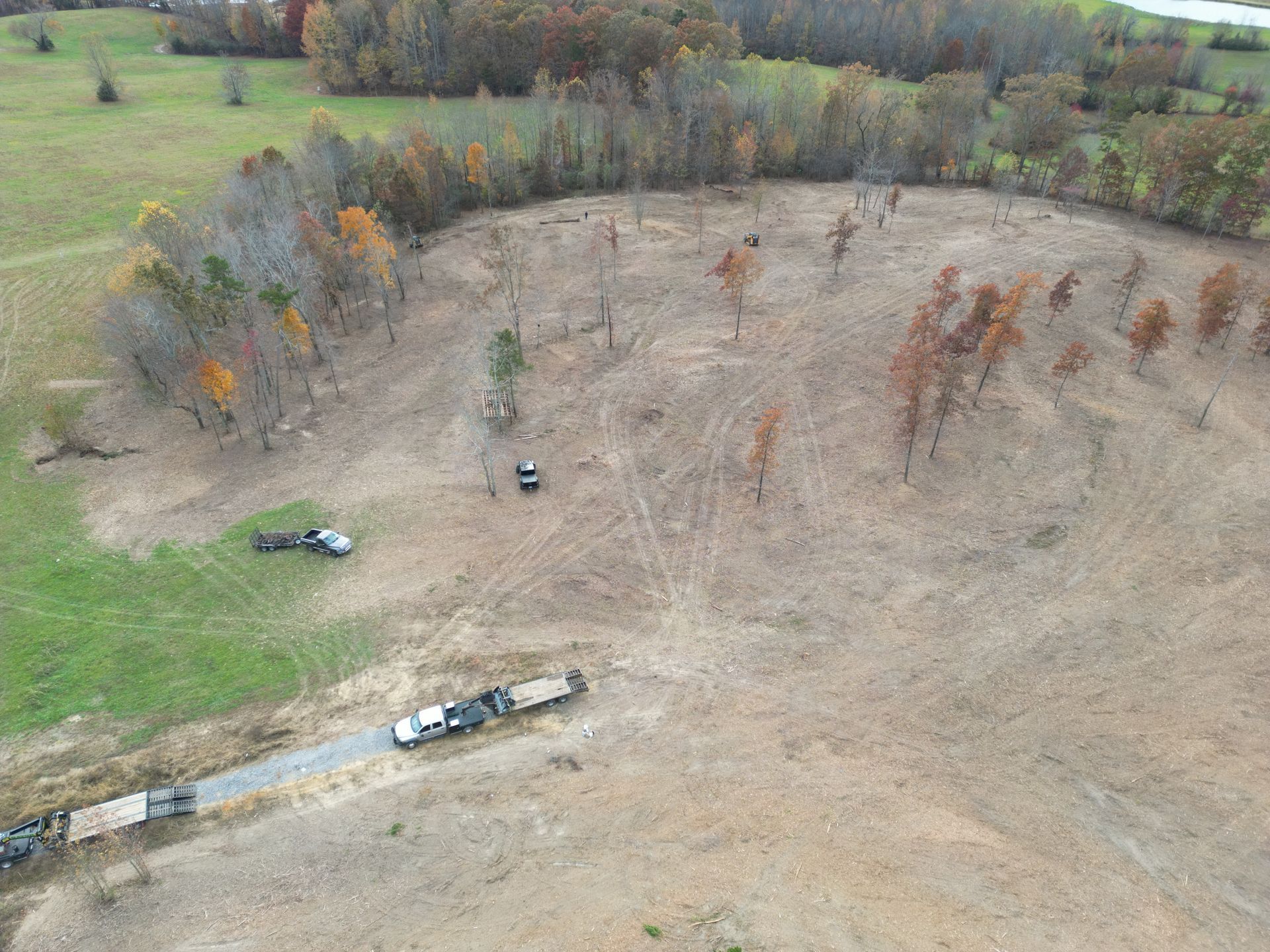 Aerial view of cleared land with trucks and sparse trees in a field, near a tree line.