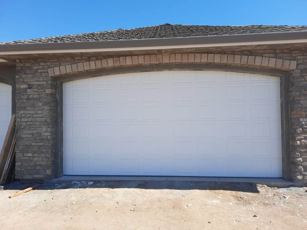 A white garage door is sitting in front of a brick building.