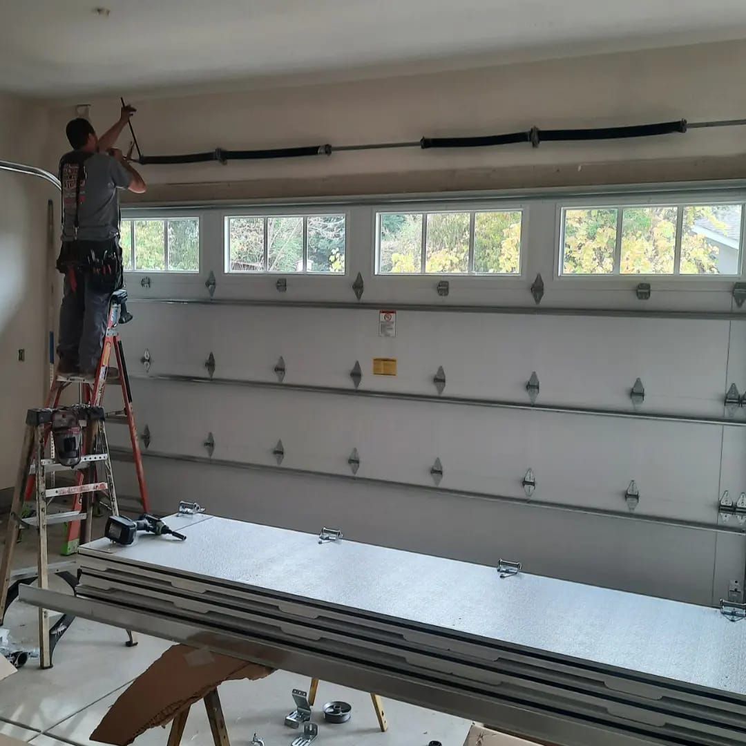 A man is standing on a ladder working on a garage door.