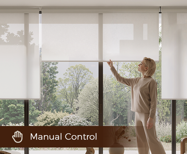 A person adjusting a white window roller shade by hand in a bright, modern room overlooking a garden.