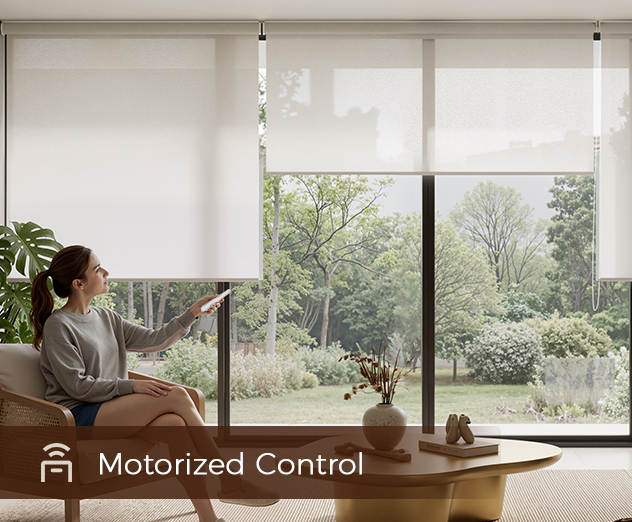 A person sits in a chair using a remote to adjust motorized roller shades in a room with a large window and garden view.