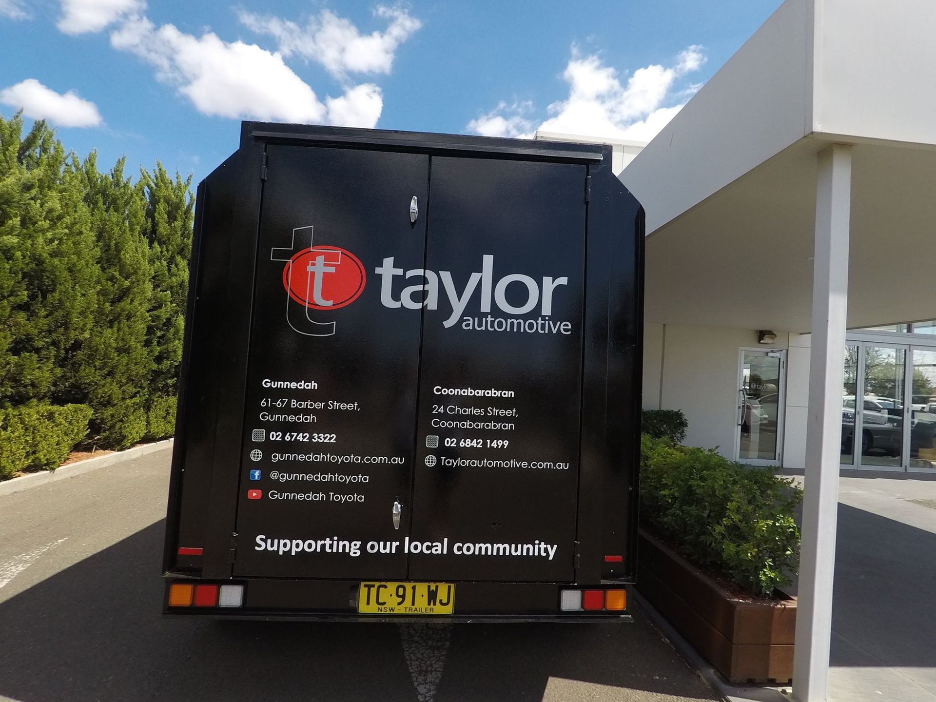 A black trailer with a wrap is parked in front of a building — McKnight Signs In Hillvue, NSW