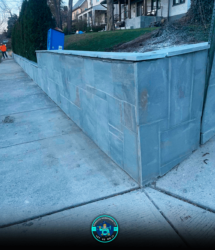 Gray stone retaining wall along a sidewalk next to a green lawn.