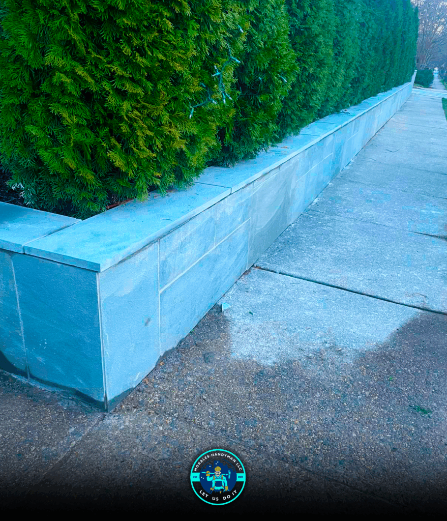 Stone wall with greenery, adjacent to a sidewalk.