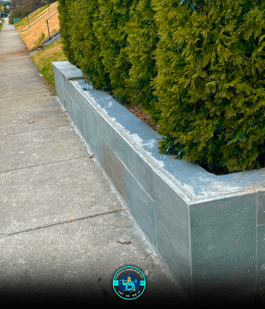 Concrete retaining wall with green hedge along sidewalk.