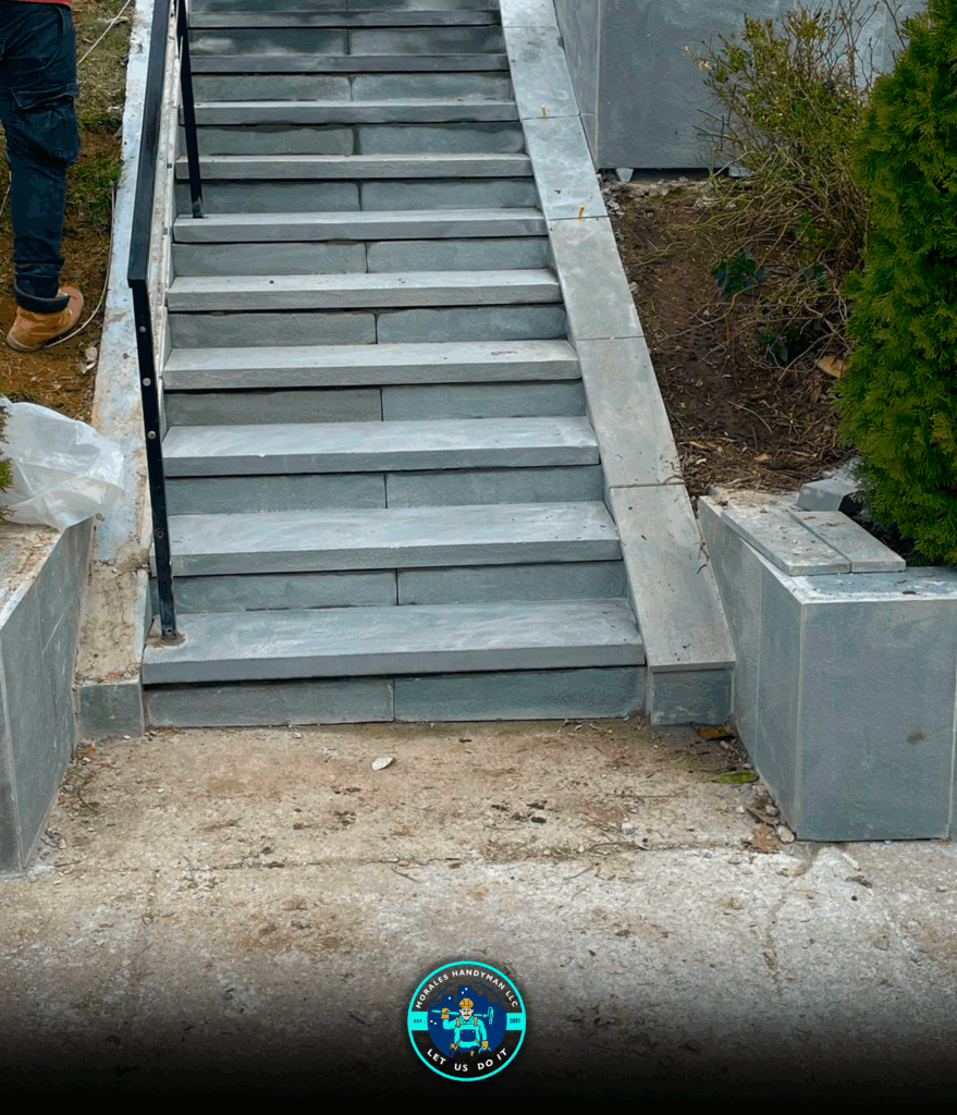 Stone staircase with a black railing, leading up to a higher level.
