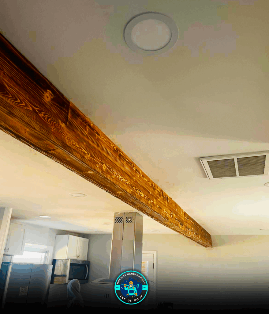 Wooden beam on a beige ceiling, with a room featuring cabinets, a microwave, and a person.