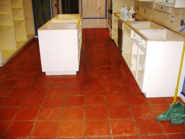 Red tile floor in a kitchen under renovation. White cabinets and shelves.