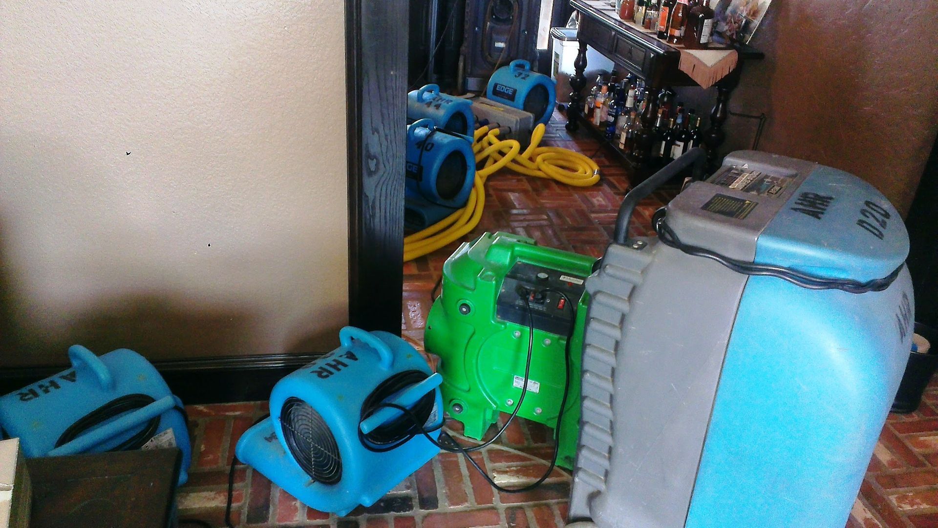 Blue and green industrial fans and a water extraction machine in a room with exposed brick flooring.