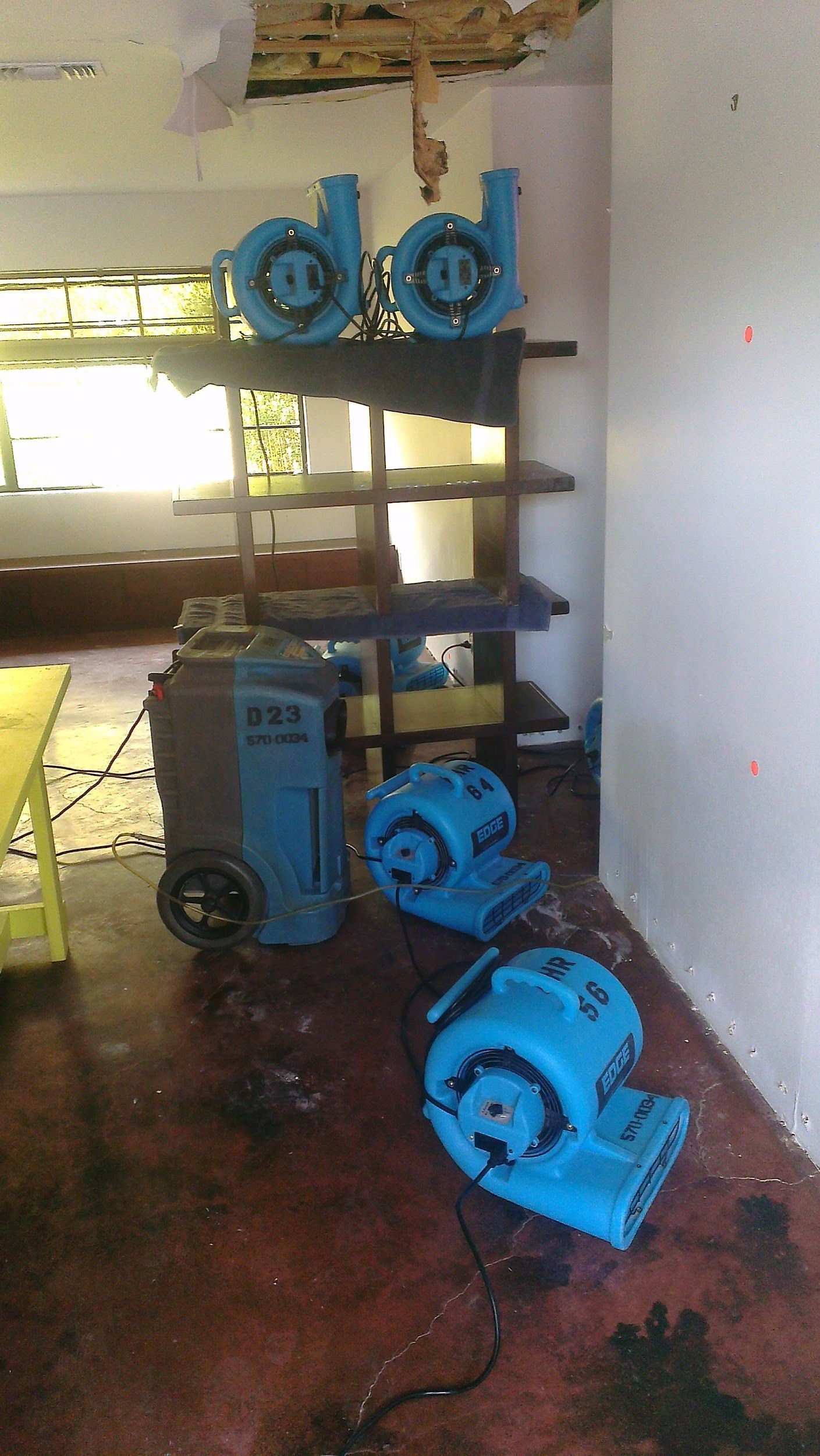 Blue water damage restoration equipment in a room with damaged ceiling and floor.
