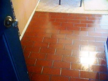 Dark red brick-like tiled floor, glossy finish. View from a doorway.