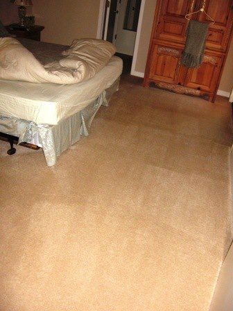 Bedroom with a bed, tan carpet, and a wooden door.