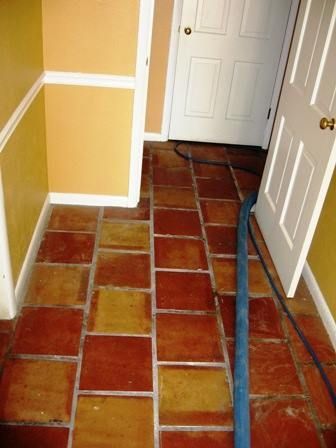 Red and tan tiled floor with blue hose, white door and trim, yellow walls.