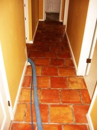 Brown tile hallway with cleaning hose. Yellow walls, white trim, and open doors.