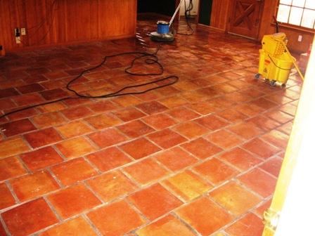 Terracotta tile floor being cleaned with industrial equipment in a wood-paneled room.